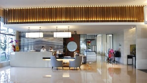 A modern reception area with a wooden slatted ceiling, a reception desk, two grey chairs, and a large window with natural light. - Formosa Naruwan Galaxy Hotel Taitung (Taitung)
