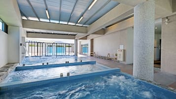 A large indoor swimming pool with multiple hot tubs, a skylight ceiling, and a view of the outdoors.