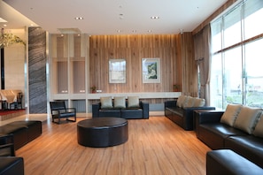 A modern lobby with wooden paneling, leather sofas, and a central ottoman.