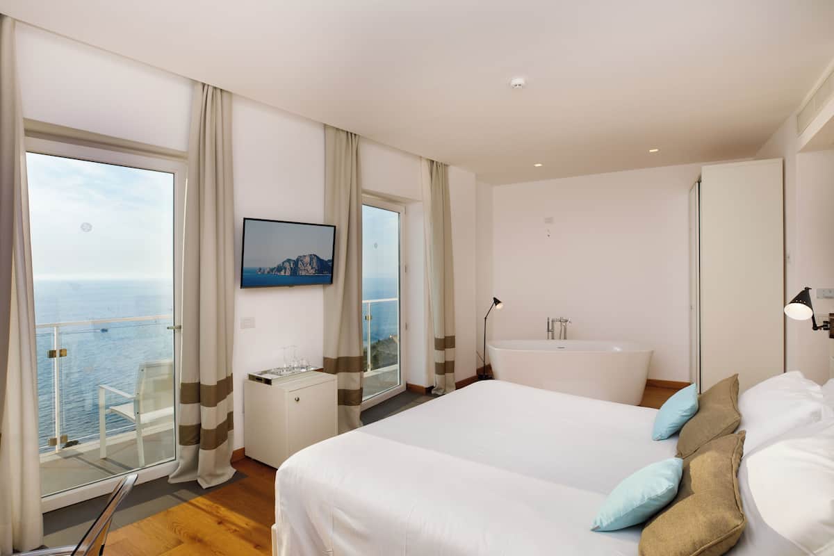 Una camera d'albergo con un letto grande, una vasca da bagno, una scrivania con una sedia e vista sul mare.