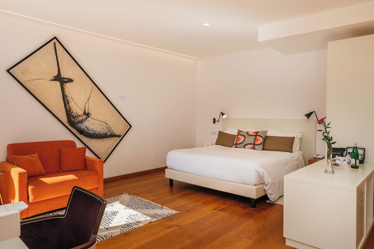 Una camera da letto moderna con un letto, un divano, una scrivania e un grande quadro astratto appeso alla parete.