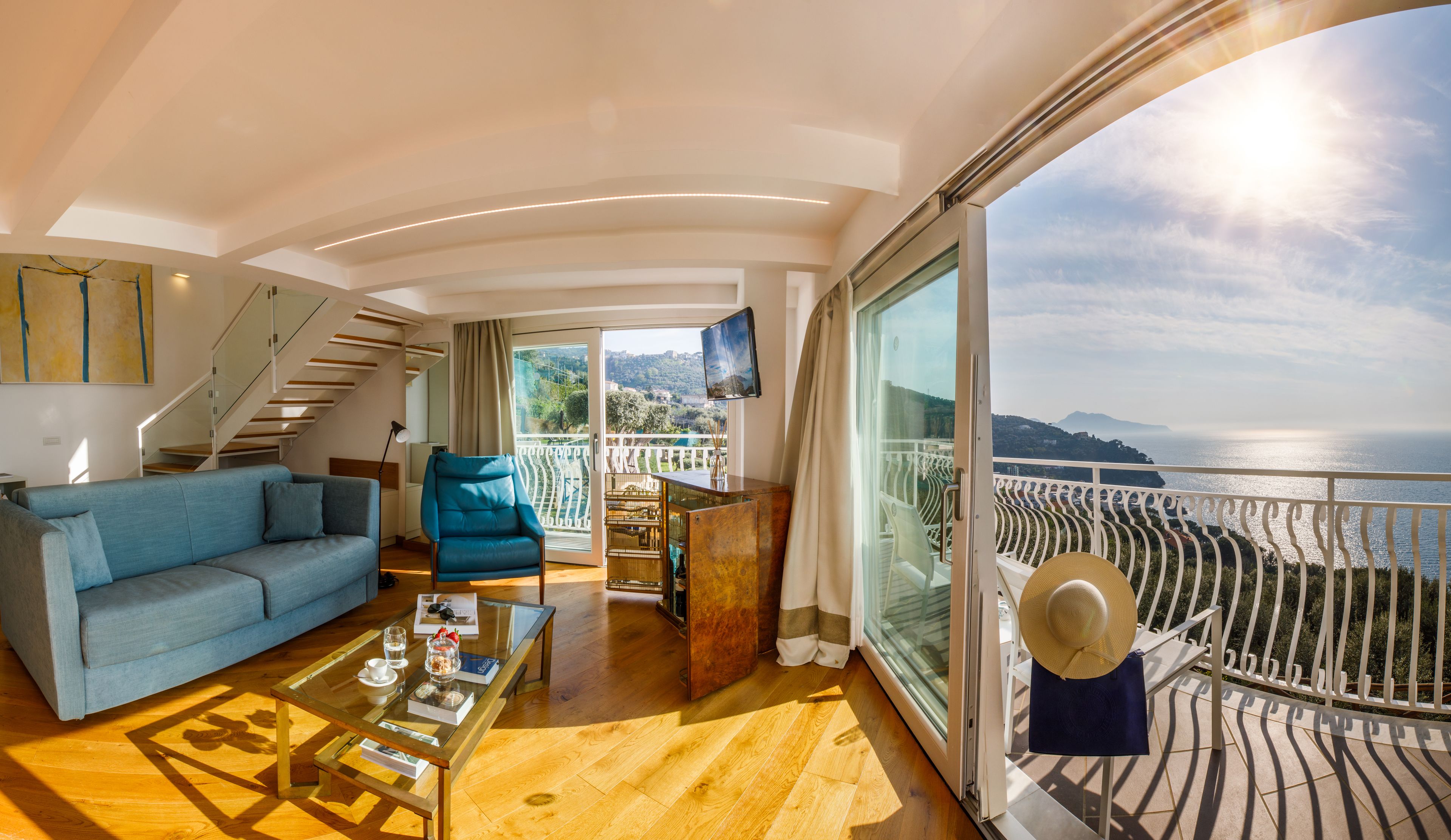 Ein modernes Interieur mit einer Couch, einem Sessel und einem Couchtisch, einer Treppe sowie einem Balkon mit Meerblick.