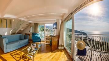 Ein modernes Interieur mit einer Couch, einem Sessel und einem Couchtisch, einer Treppe sowie einem Balkon mit Meerblick.