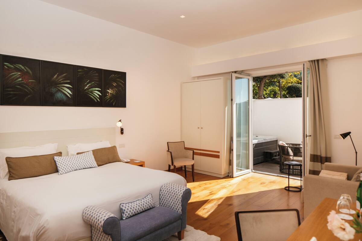 Camera moderna con un letto grande, un divano, un tavolo da pranzo e una porta scorrevole in vetro che dà su un balcone.