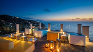 A rooftop terrace with seating and tables, overlooking a coastal landscape at dusk. - Villa Fiorella Art Hotel (Massa Lubrense)