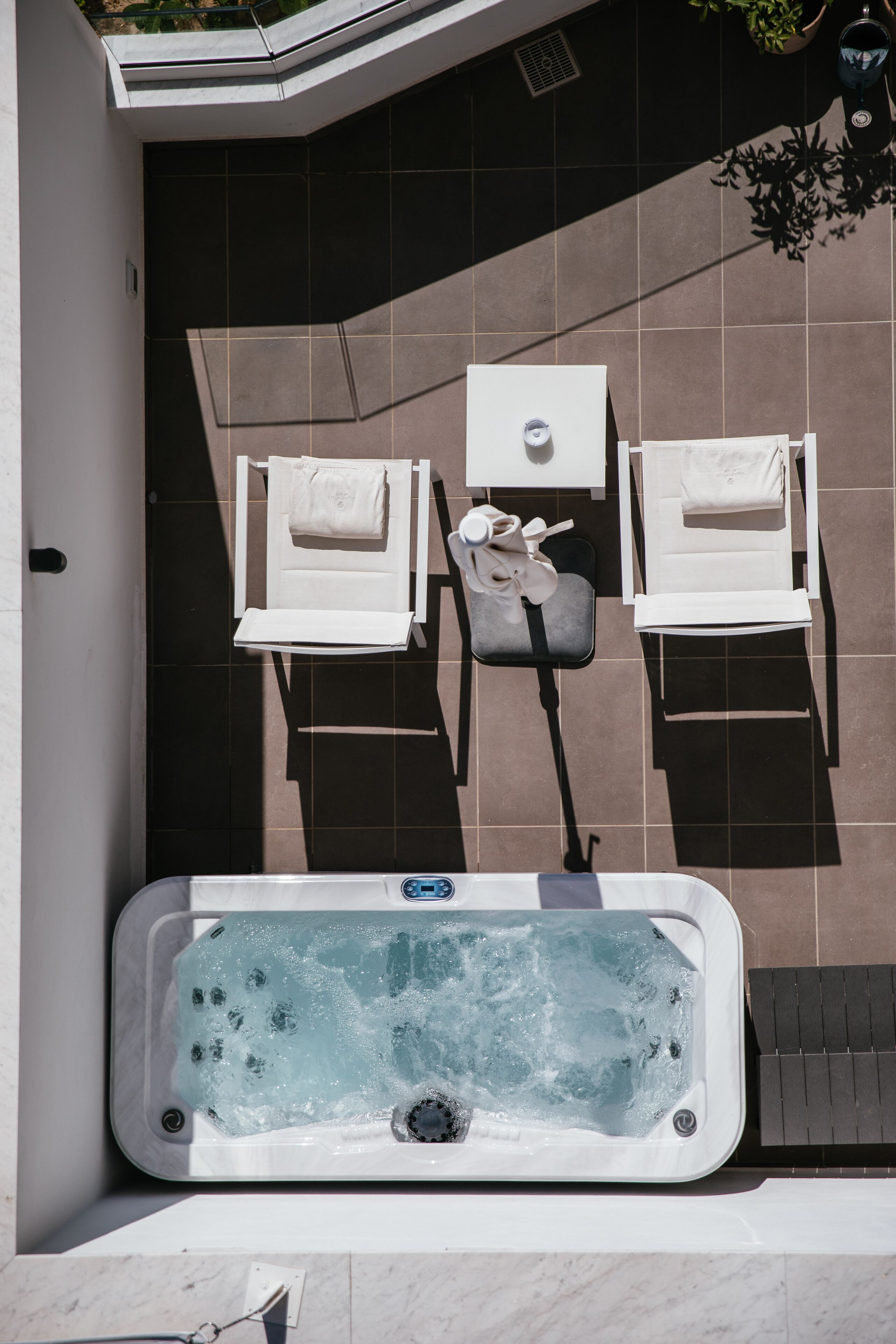 A spa area with a hot tub, two white lounge chairs, and a small table with a towel and a bag.