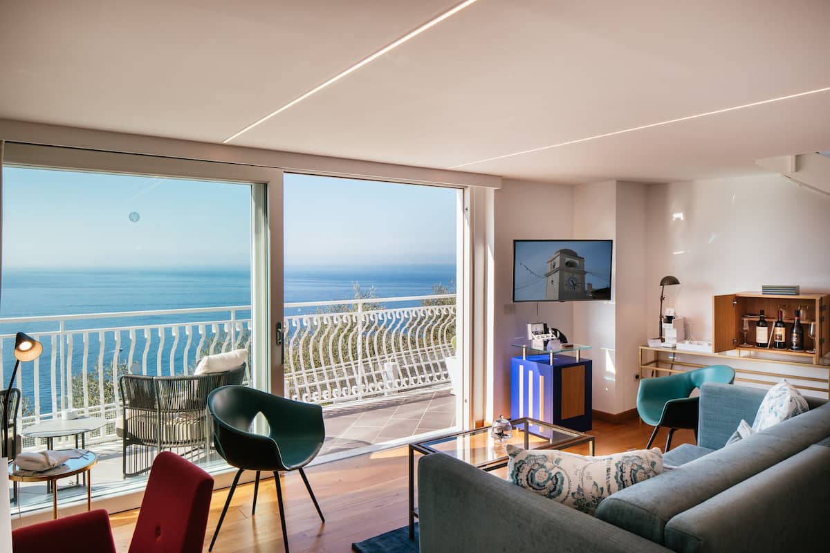 Un soggiorno moderno con balcone vista mare, dotato di divano, poltrone e zona pranzo.