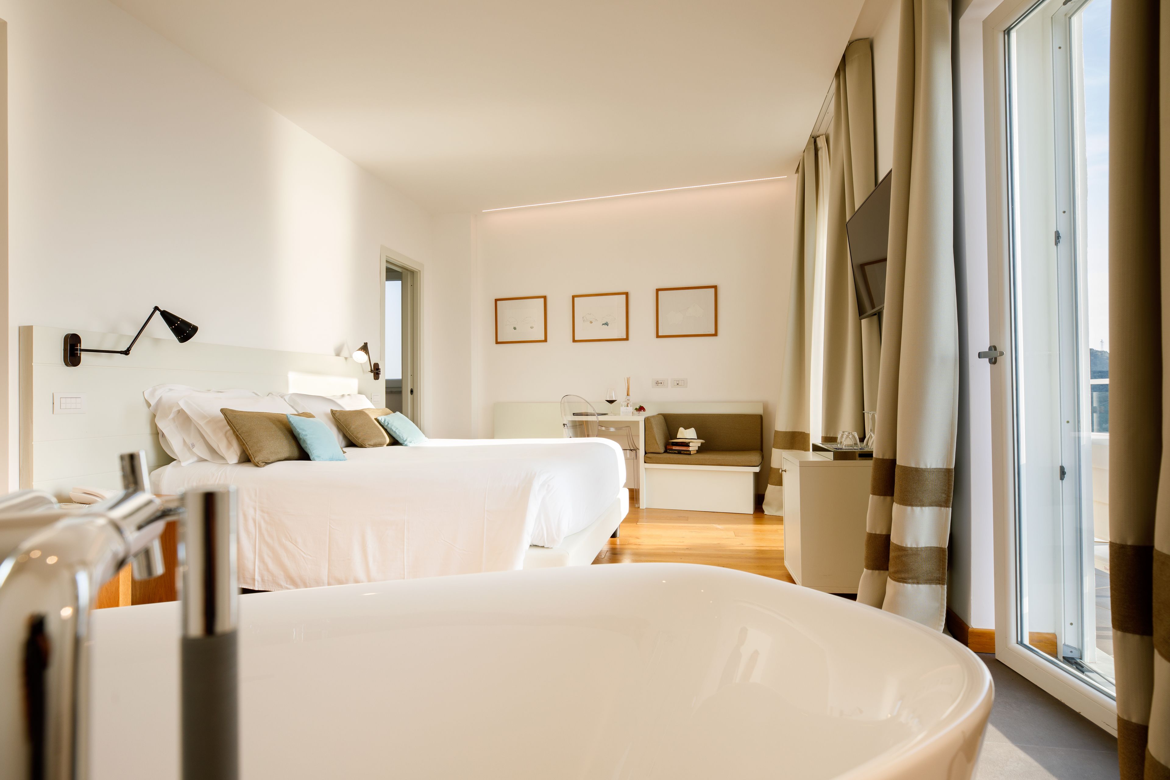 A hotel room with two beds, a desk, a chair, a window with curtains, and framed pictures on the wall.