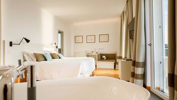A hotel room with two beds, a desk, a chair, a window with curtains, and framed pictures on the wall.