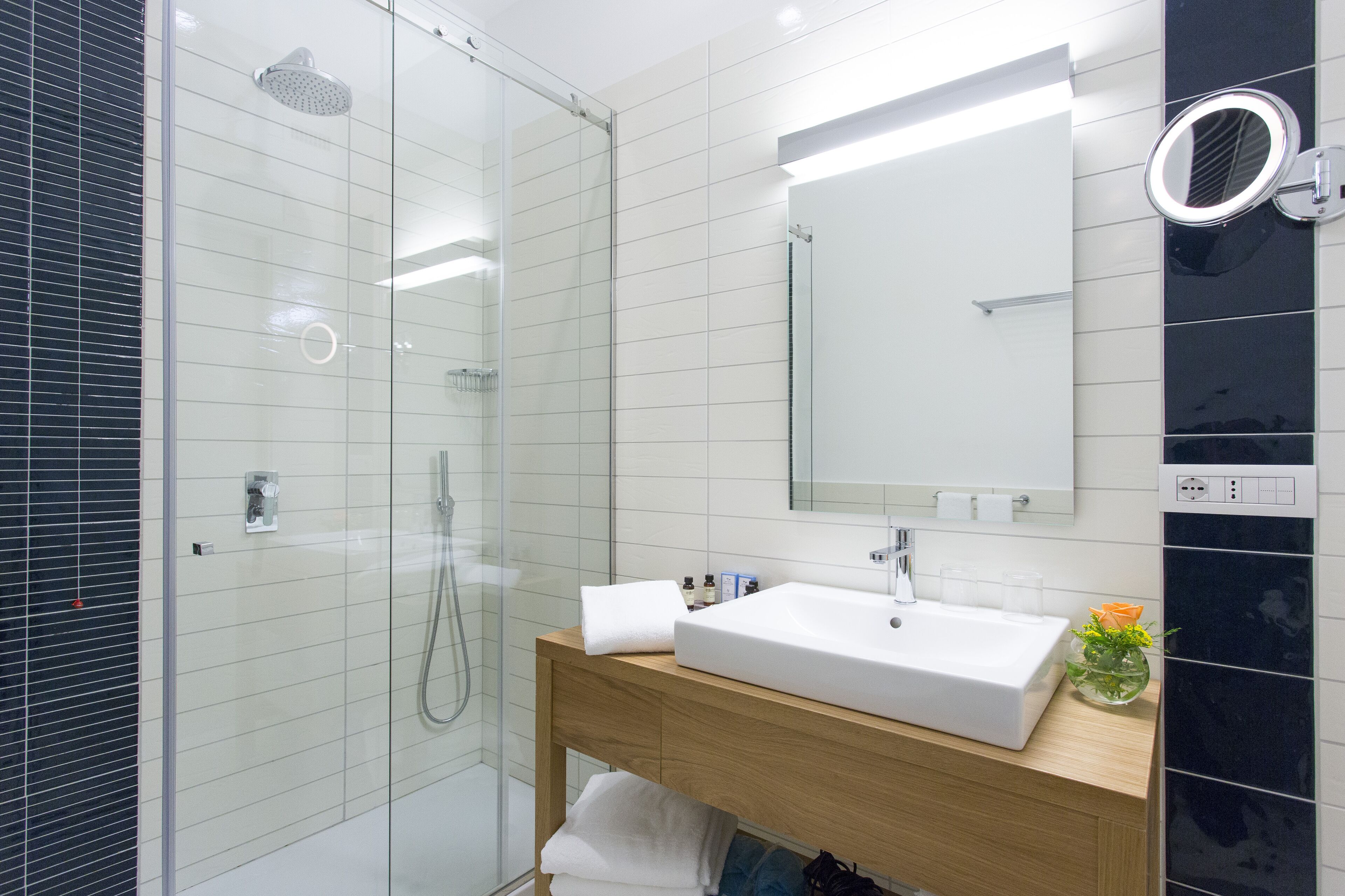 Une salle de bain moderne avec une douche à parois de verre, un lavabo blanc et un miroir doté d’un éclairage circulaire.