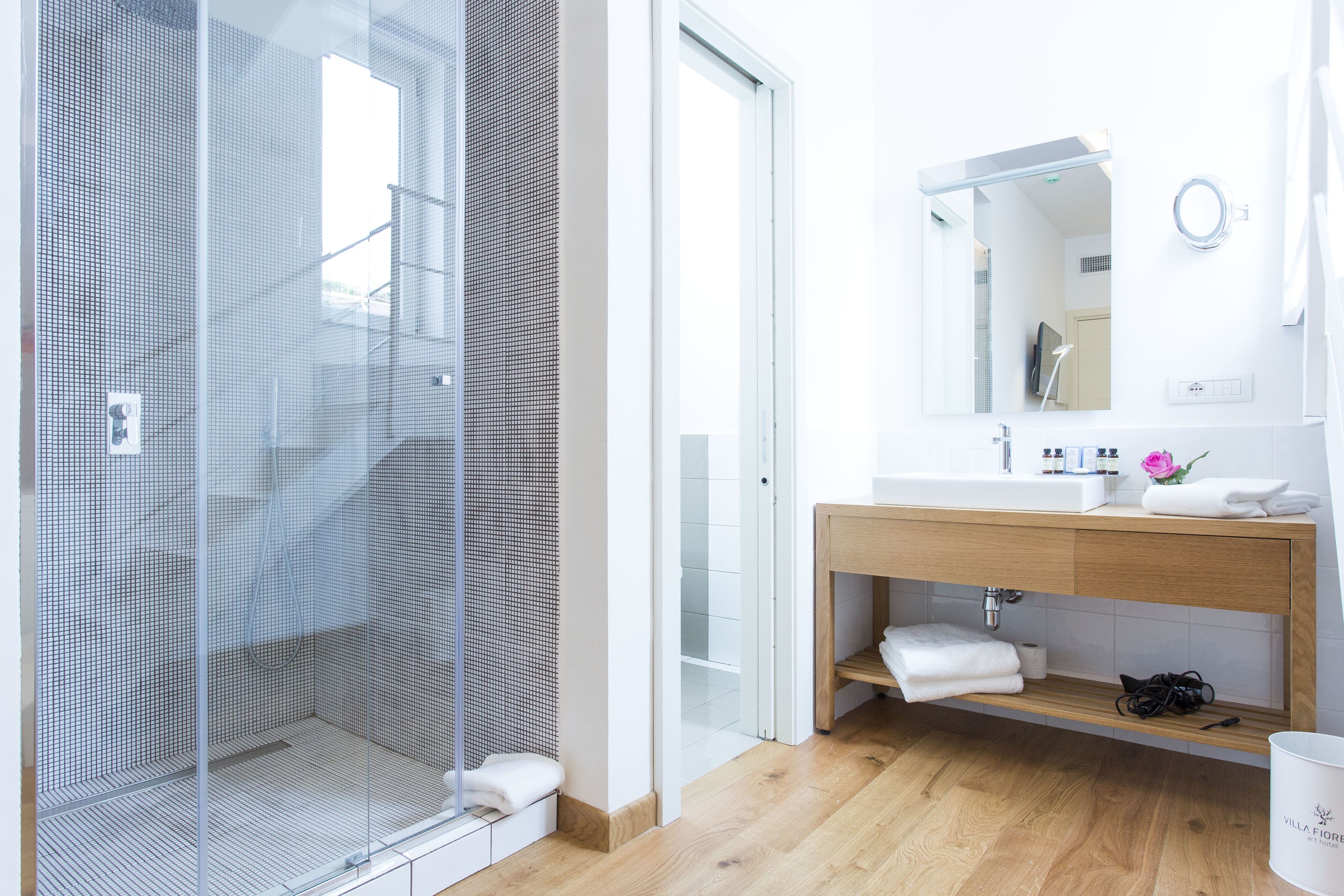 Un baño moderno con ducha acristalada, tocador de madera con espejo y lavamanos blanco.