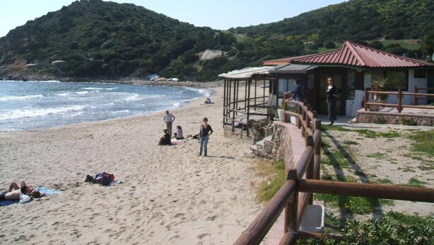 Una playa con una cerca de madera, una estructura cubierta y gente relajándose.