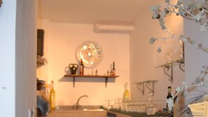 Una cocina con un jarrón blanco sobre una mesa, una estantería con botellas y una planta colgante.