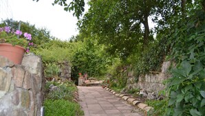 Un sendero de piedra que atraviesa un jardín exuberante con plantas en macetas y abundante vegetación.