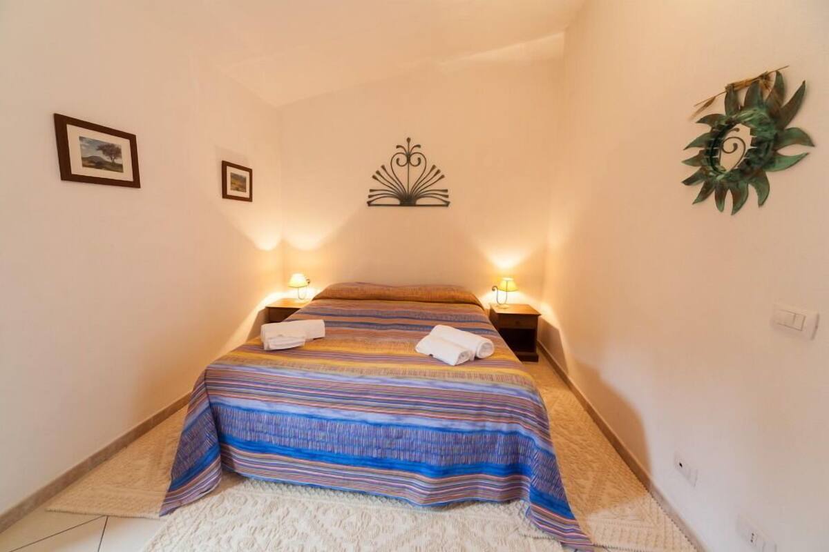 Un dormitorio con cama, dos mesitas de noche y luces fijadas a la pared.