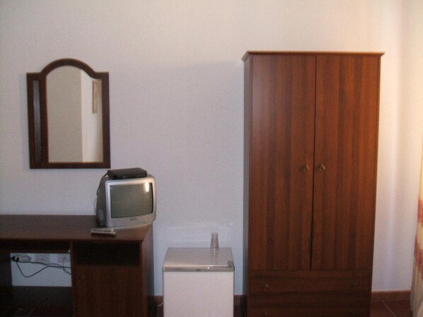 Una habitación con un armario de madera, un pequeño mueble blanco y un televisor sobre un escritorio de madera.