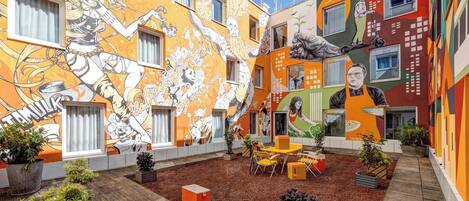 A courtyard with colorful murals, outdoor seating, and potted plants.