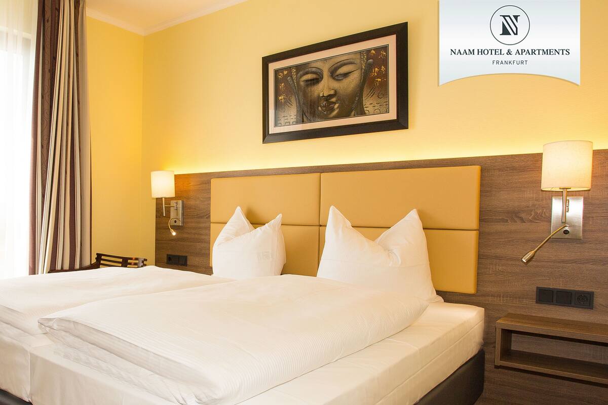Habitación de hotel con una cama grande, dos lámparas de noche, una obra de arte enmarcada sobre la cama y un cartel del Hotel & Apartamentos Naam.