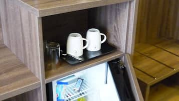A compact kitchenette with a coffee maker, a bottle of water, and a refrigerator containing snacks and beverages.