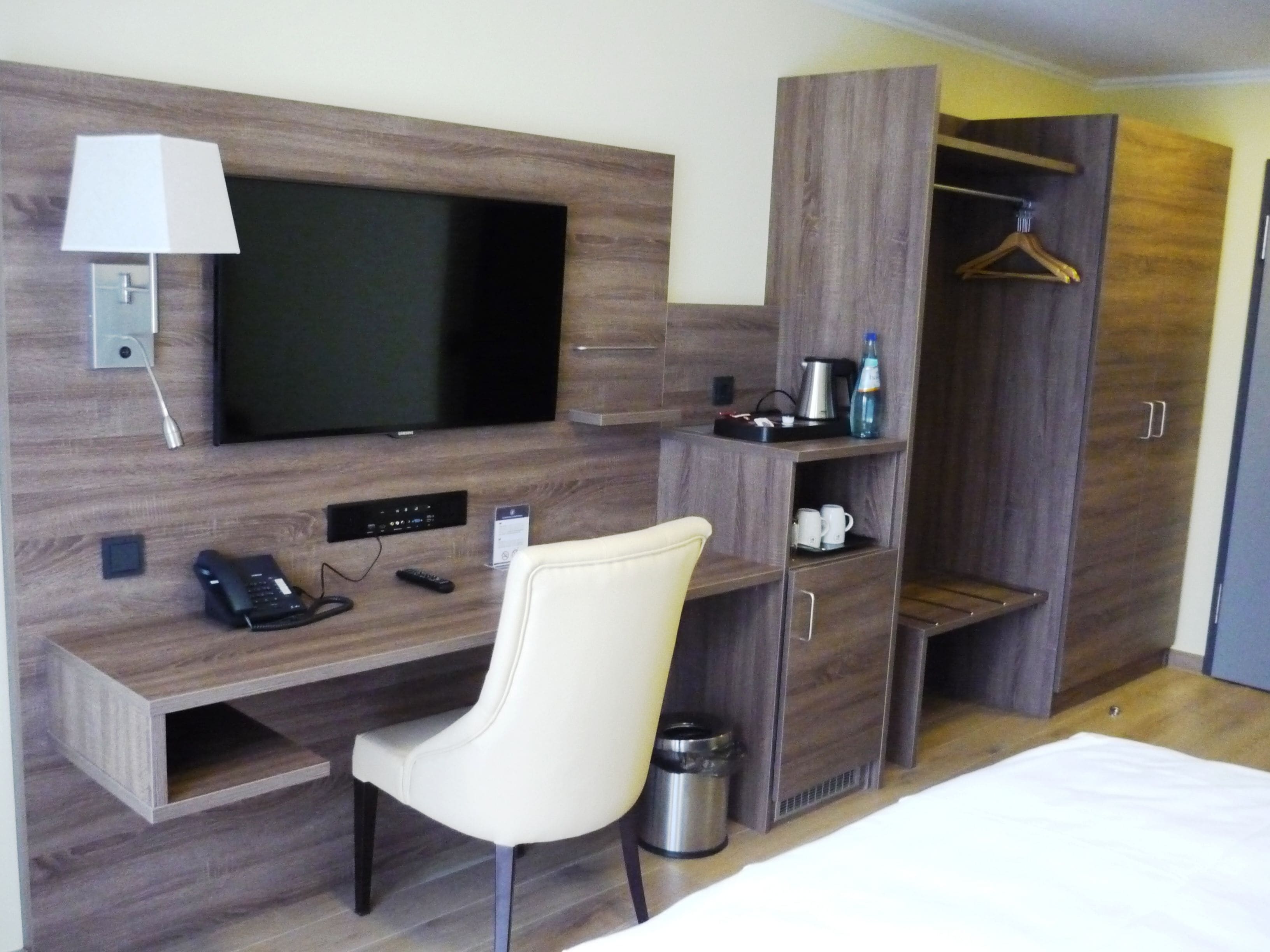 Hotellihuone, jossa on puinen työpöytä, televisio, tuoli, vaatekaappi ja sänky.