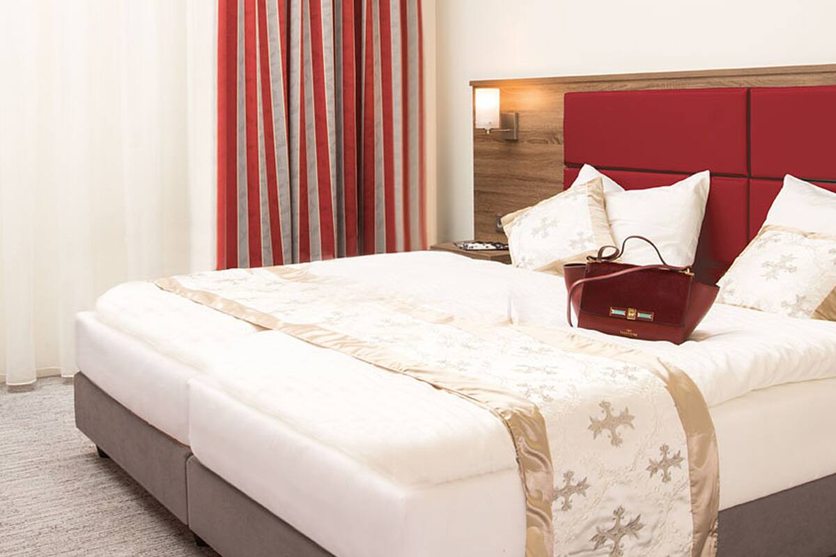 Una habitación de hotel con una cama grande, cabecera roja y una mesita de noche con lámpara.