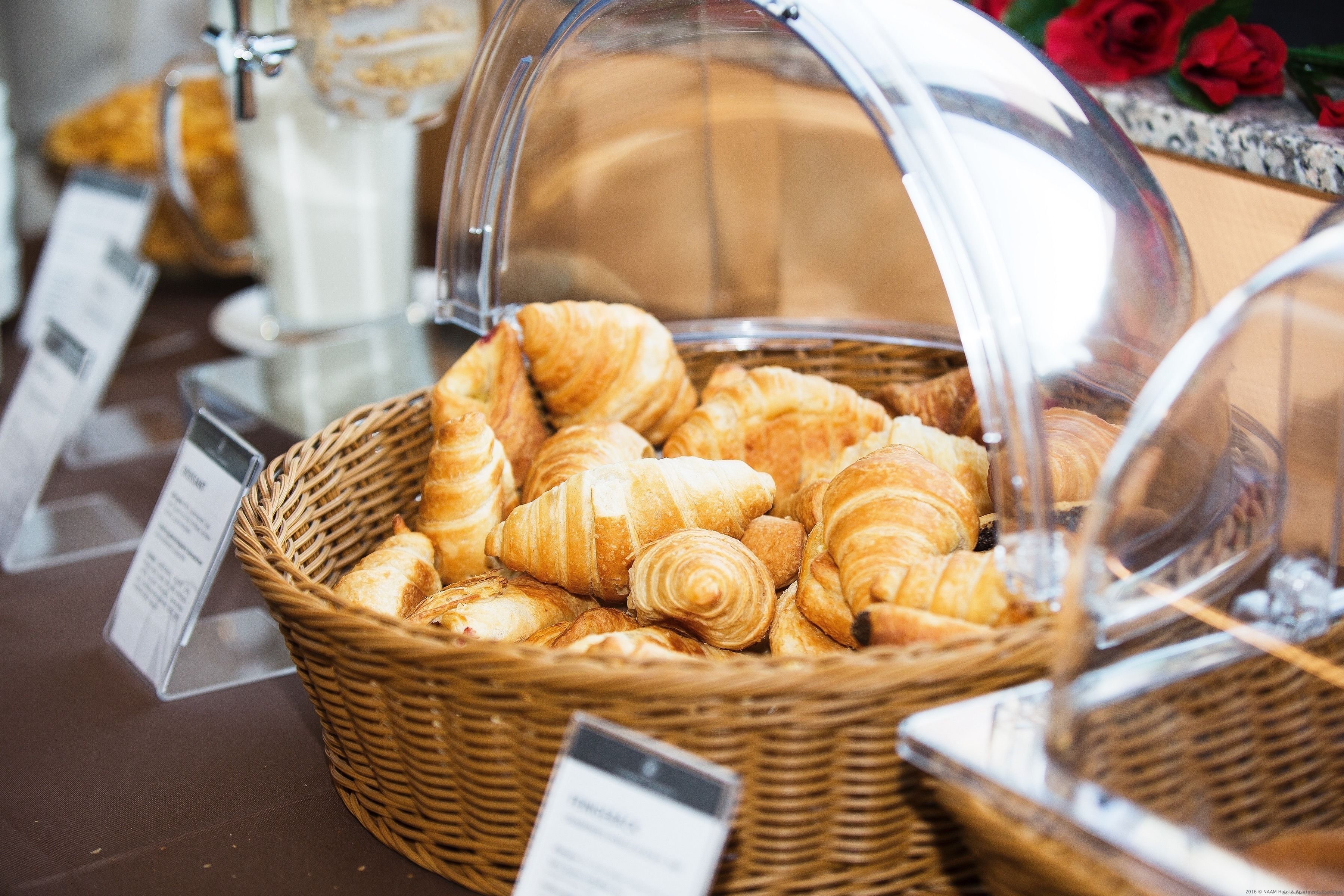 Una exhibición de croissants en una cesta de mimbre con una cubierta de cristal.