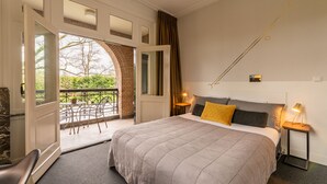 A bedroom with a large bed, a balcony, a view of greenery, and a small table with a lamp. - Boutique Hotel Het Scheepshuys (Breda)