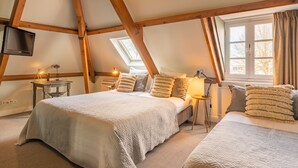 A bedroom with two beds, wooden beams, a TV, a window with curtains, and a lamp. - Boutique Hotel Het Scheepshuys (Breda)