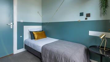 A bedroom with a bed, a bedside table with a lamp, and a wall-mounted shelf.