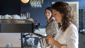 Een koffieapparaat met een kop en schotel, een metalen kan en een persoon die koffie inschenkt.