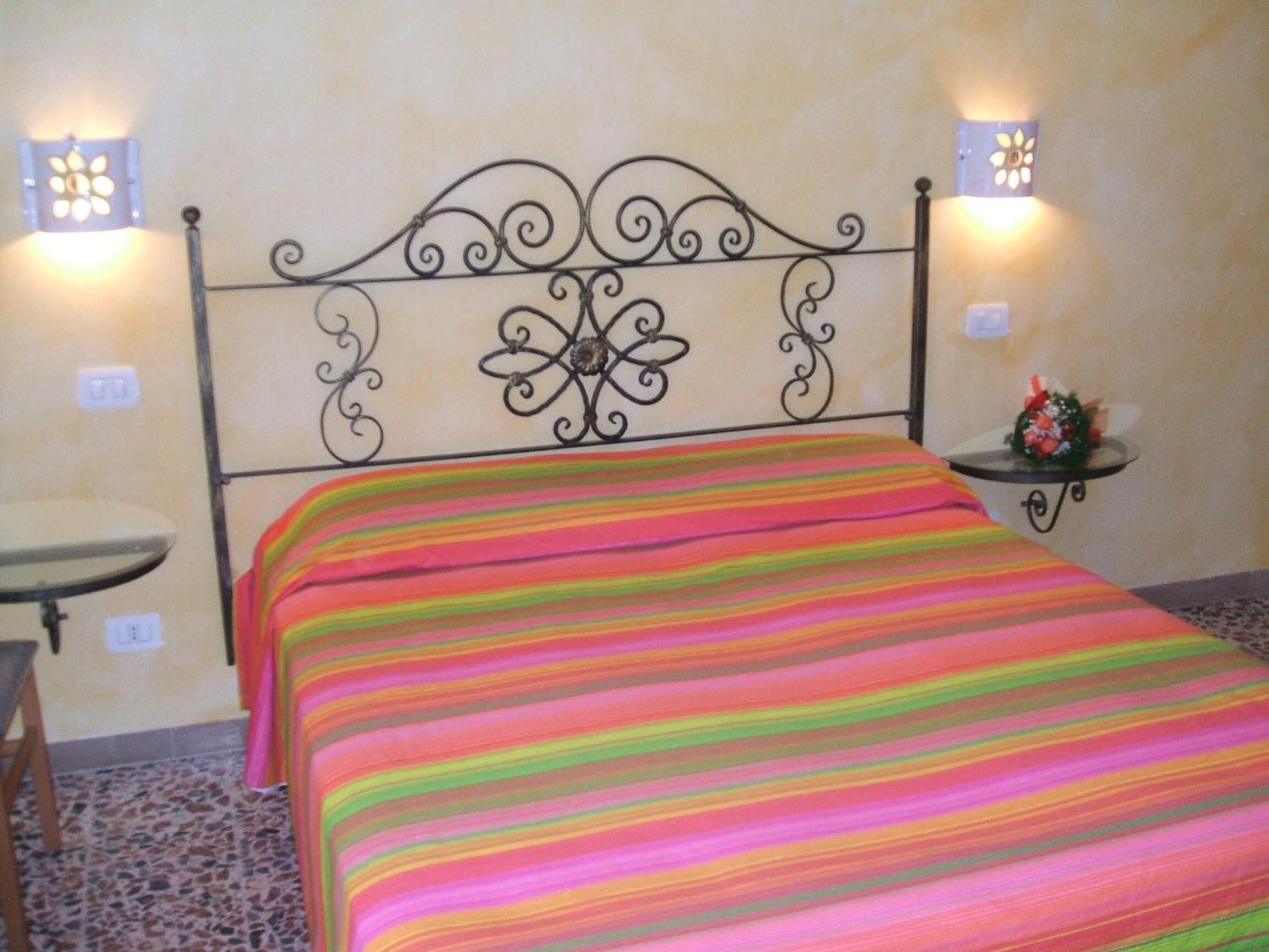 A bed with a colorful striped bedspread, a decorative metal headboard, and two wall-mounted light fixtures.