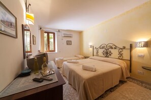 Habitación de hotel con dos camas, un escritorio con lámpara, una ventana y aire acondicionado instalado en la pared.