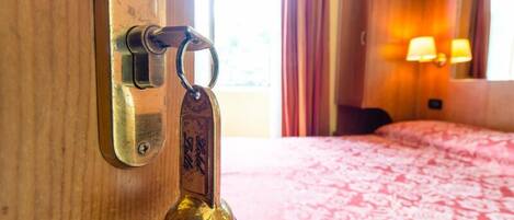 A hotel room with a wooden door, a keychain, a bed with a patterned bedspread, and a wall-mounted lamp.