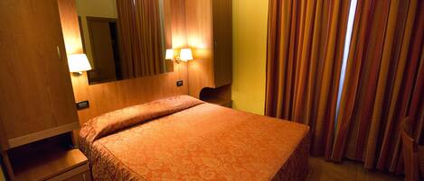 A hotel room with a bed, a nightstand, a mirror, and curtains.