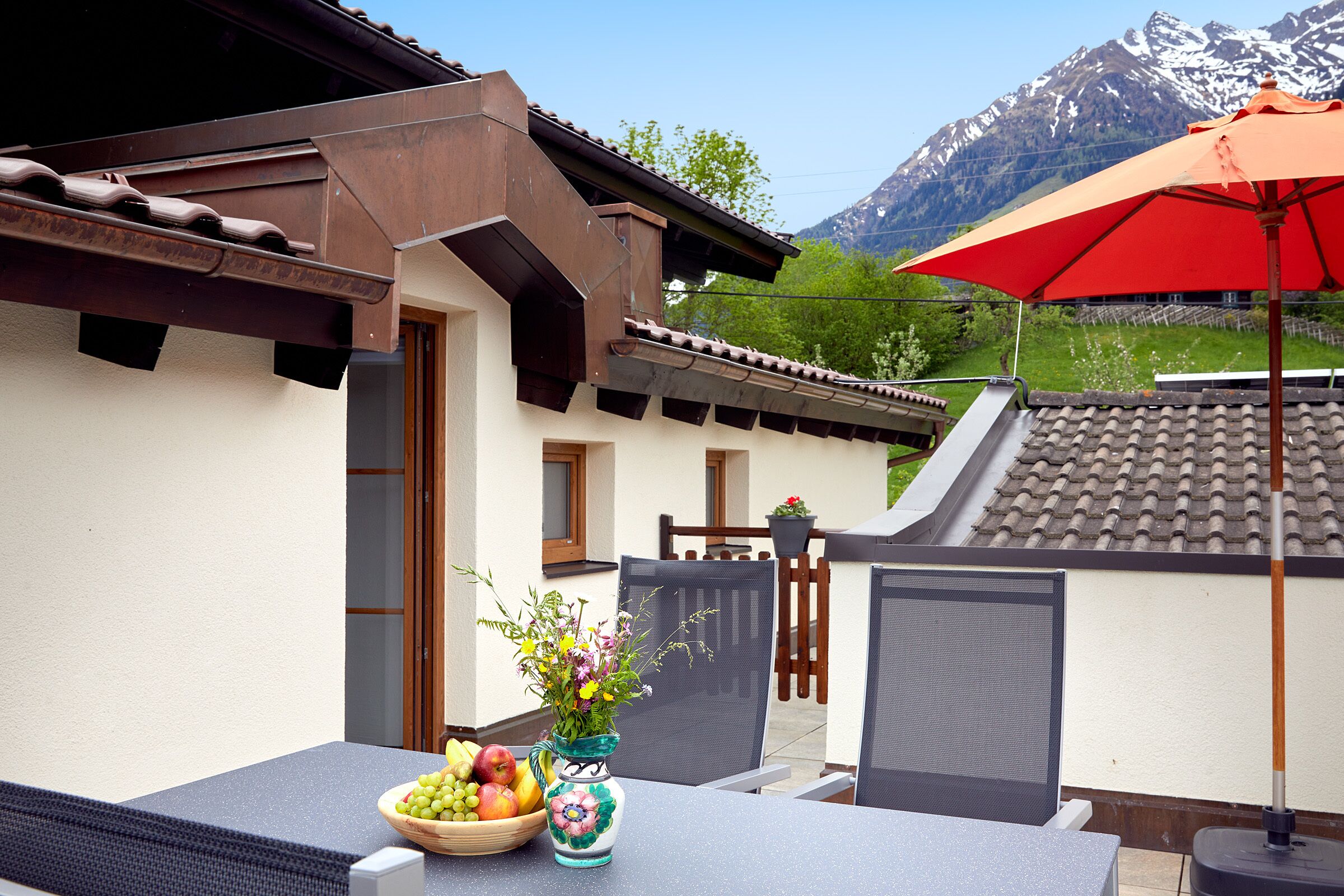 Eine Terrasse mit Tisch, einer Obstschale und einem Blumenstrauß.