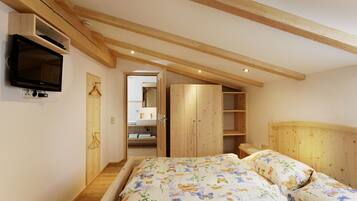 A bedroom with a wooden ceiling, a bed with floral bedding, a TV mounted on the wall, and a wooden wardrobe.