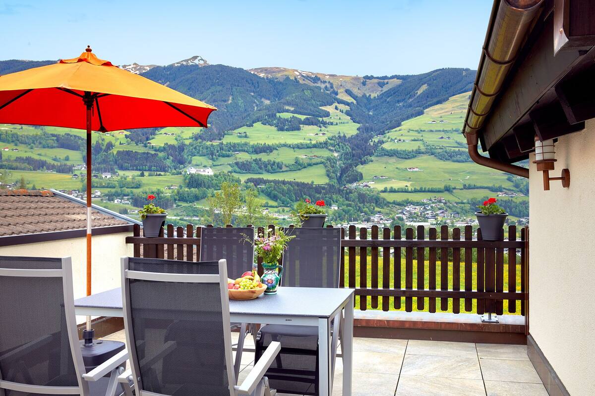 A balcony with a table and chairs, a red umbrella, and potted plants.