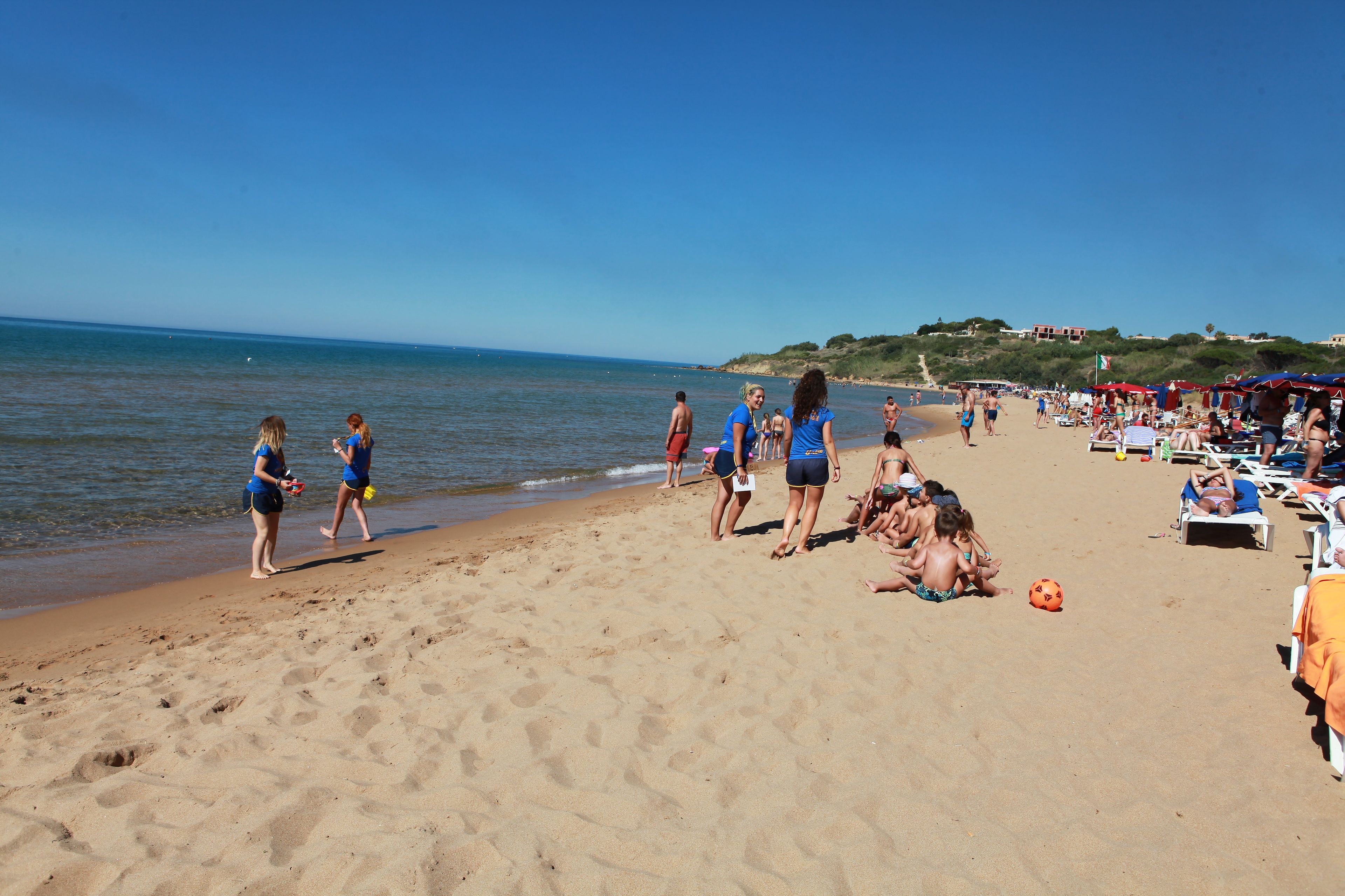 A beach with people walking and sunbathing, umbrellas, and beach chairs.