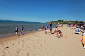 A beach with people walking and sunbathing, umbrellas, and beach chairs.