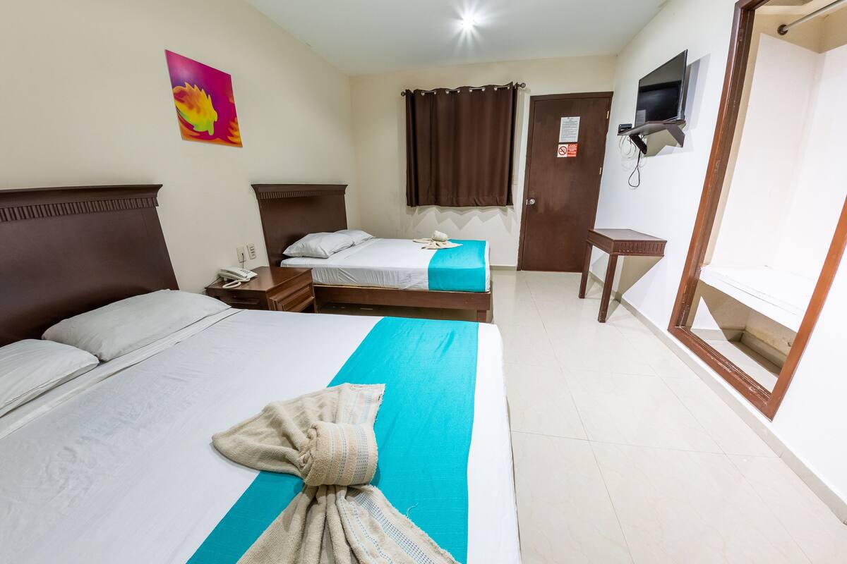 Habitación de hotel con dos camas, un televisor montado en la pared, una mesita y una puerta con un letrero.
