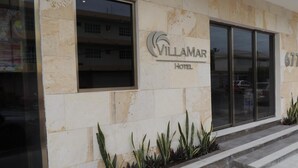 The exterior of the Villamar Hotel with a stone facade, large windows, and a small planter with plants. - Hotel Villamar (Veracruz)