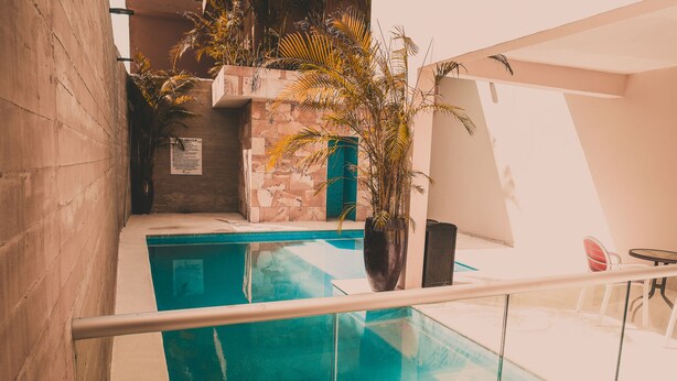 A modern indoor pool area with a glass railing, a stone wall, and a potted plant. - Hotel Villamar (Veracruz)