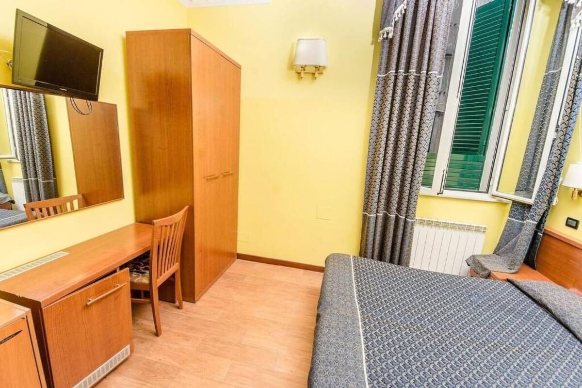 A hotel room with a bed, a desk, a chair, a television, a wardrobe, and a window with curtains.
