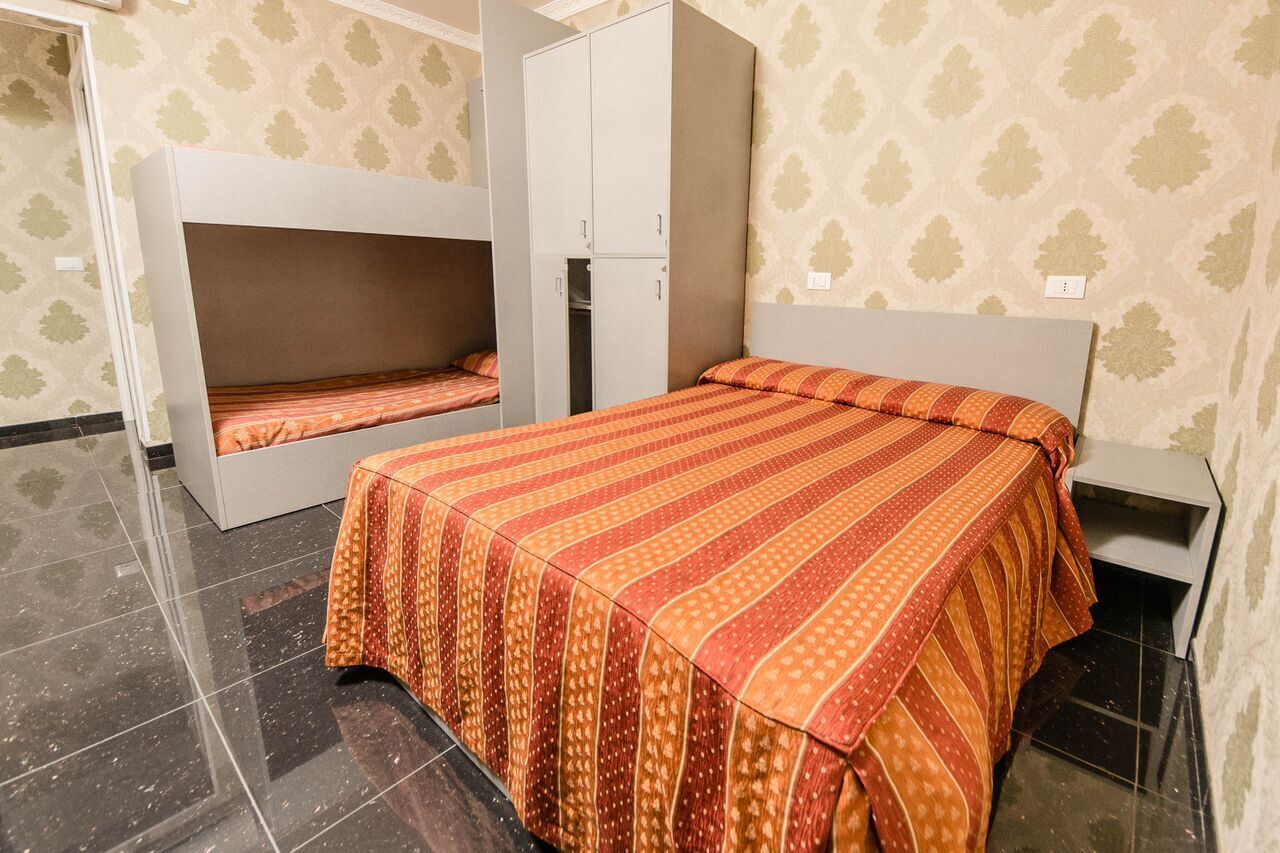 A room with bunk beds, a single bed with a patterned bedspread, a wardrobe, and a small bedside table.