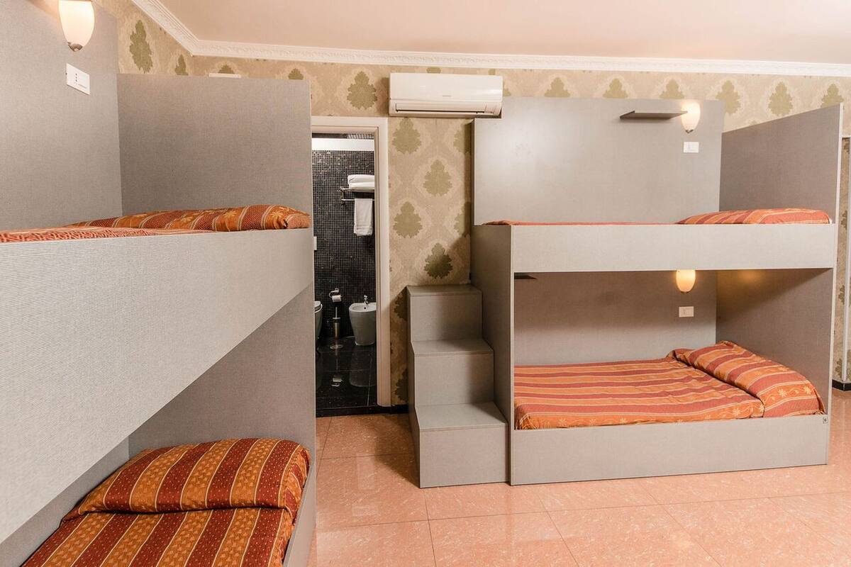 A dormitory room with bunk beds, a small kitchenette, and an air conditioning unit.