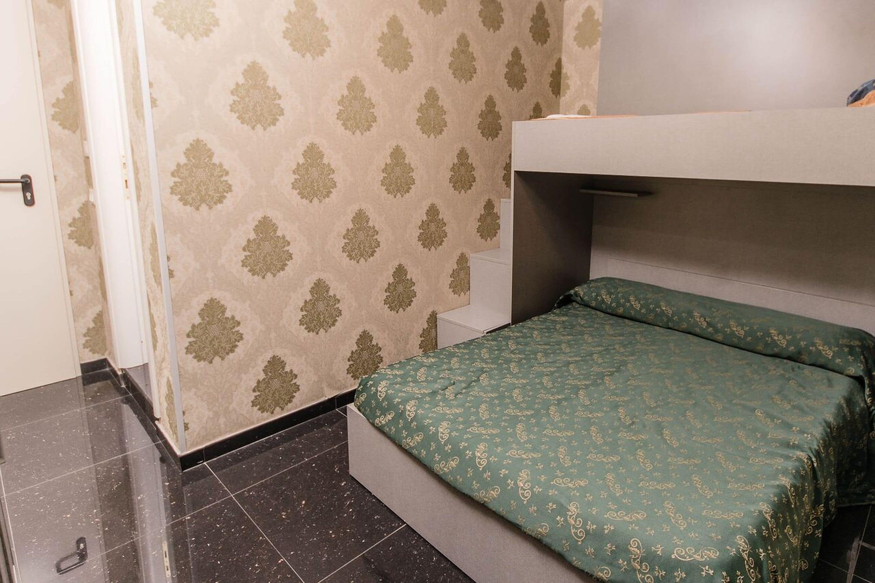 A small, compact room with a bunk bed, a patterned wall, and a tiled floor.