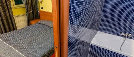 A small, compact room with a bed, a shower area, and a toilet.