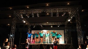 Un escenario con un grupo de personas actuando, rodeado por una estructura metálica de entramado.