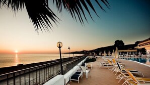 Un complejo turístico frente al mar con piscina, tumbonas y vistas a la puesta de sol sobre el océano.