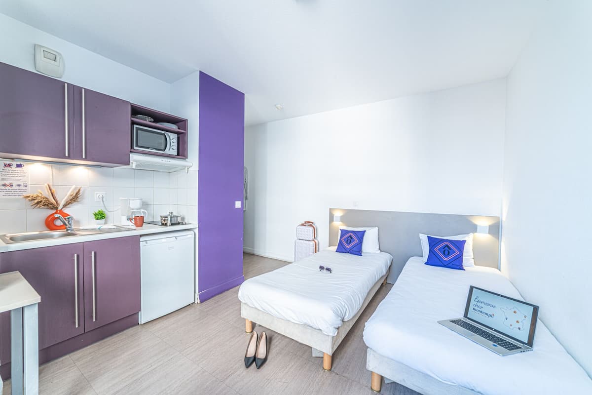 Ein kleines Hotelzimmer mit Küchenzeile, zwei Betten und einem Laptop auf einem Bett.